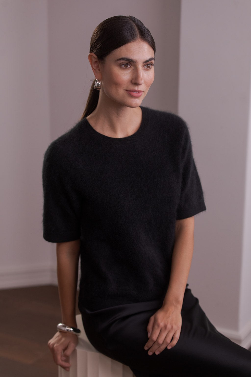 Nainen, jonka päällä on Original Storyn lyhythihainen kashmirneule, jossa harjattu pörröinen pinta, väri black