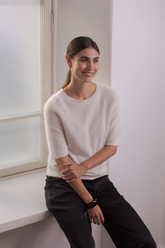 Nainen, jonka päällä on Original Storyn valkoinen lyhythihainen kashmirneule sekä mustat satiinihousut.