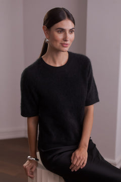 Nainen, jonka päällä on Original Storyn lyhythihainen kashmirneule, jossa harjattu pörröinen pinta, väri black