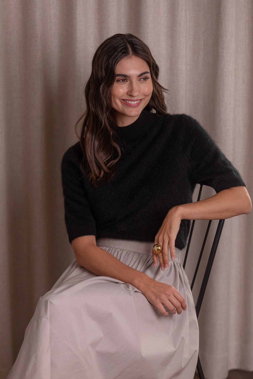 Nainen, jonka päällä on Original Storyn musta lyhythihainen puolipoolokauluksellinen kashmirneule ja puuvillahame.